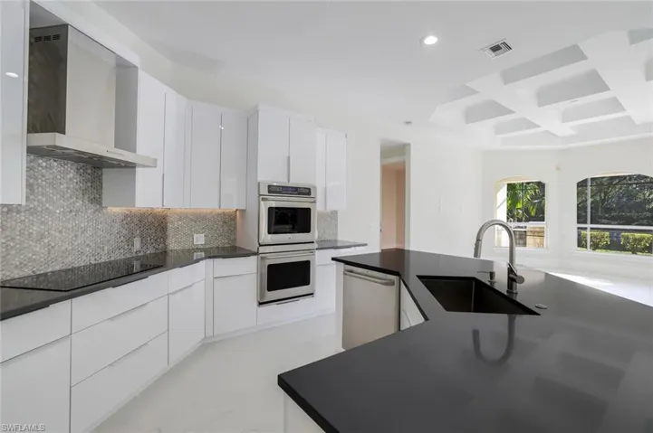 Kitchen with sink, white cabinetry, stainless steel appliances, coffered ceiling, and wall chimney exhaust hood