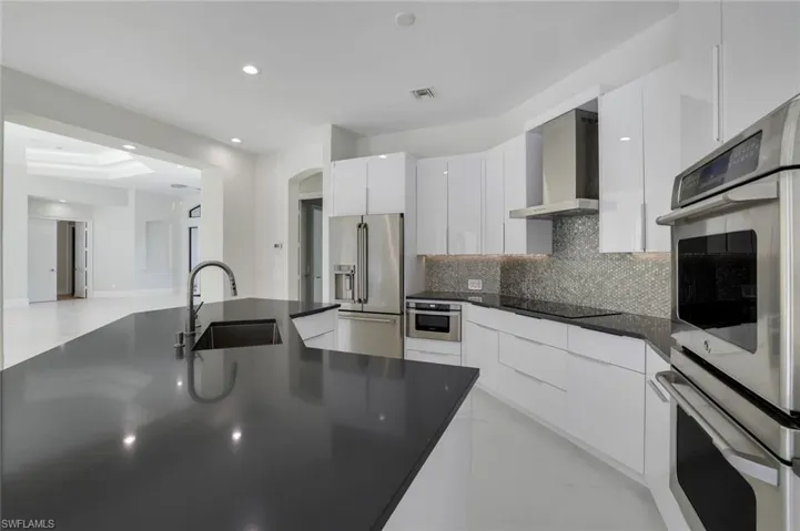 Kitchen with sink, stainless steel appliances, white cabinets, decorative backsplash, and wall chimney exhaust hood