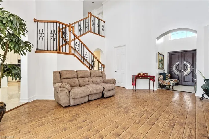 Living area featuring a towering ceiling, light wood-style flooring, arched walkways, and stairs