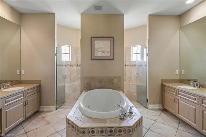 Bathroom featuring a stall shower, two vanities, a tub with jets, and baseboards