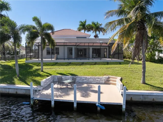 Rear view of property with a lanai, a patio area, a lawn, and a water view