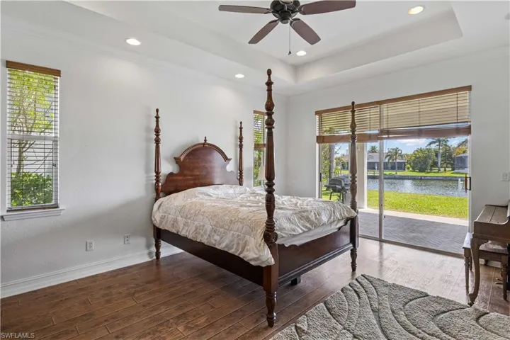 Bedroom featuring access to exterior, a raised ceiling, wood finished floors, ornamental molding, and a water view