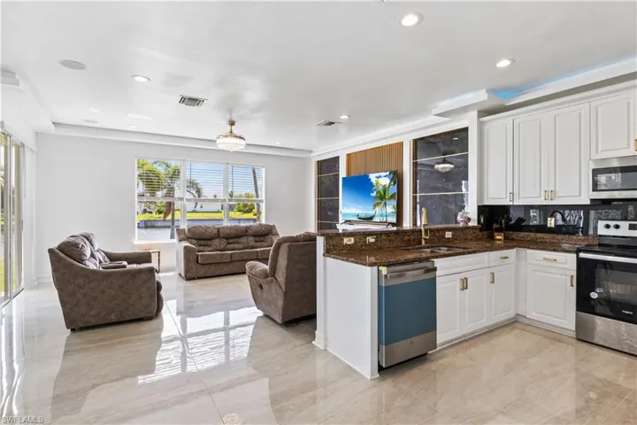 Kitchen featuring stainless steel appliances, open floor plan, a sink, white cabinets, and a peninsula