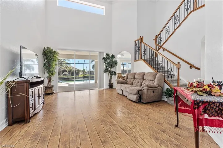 Living room featuring arched walkways, a high ceiling, light wood-type flooring, and stairs