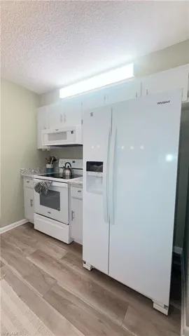 Kitchen featuring white appliances, light wood finished floors, white cabinetry, and a textured ceiling
