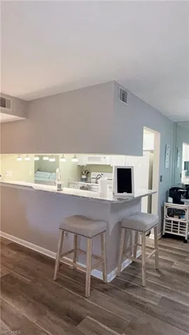 Kitchen with dark wood finished floors, a breakfast bar area, white appliances, and white cabinets
