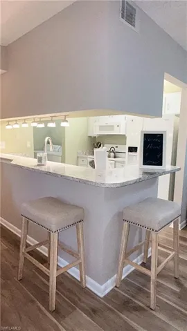 Kitchen with a kitchen bar, dark wood-type flooring, white appliances, lofted ceiling, and light stone counters