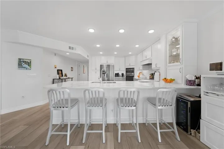 Kitchen featuring kitchen peninsula, appliances with stainless steel finishes, beverage cooler, light hardwood / wood-style flooring, and white cabinets