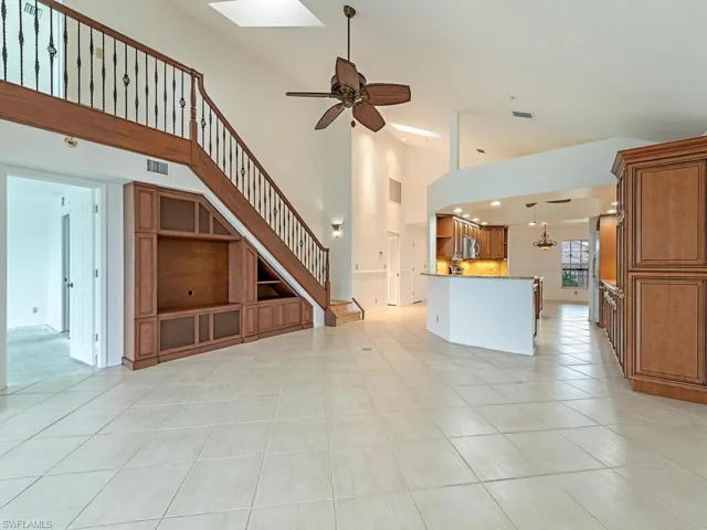 Unfurnished living room featuring ceiling fan, light tile patterned floors, and a high ceiling