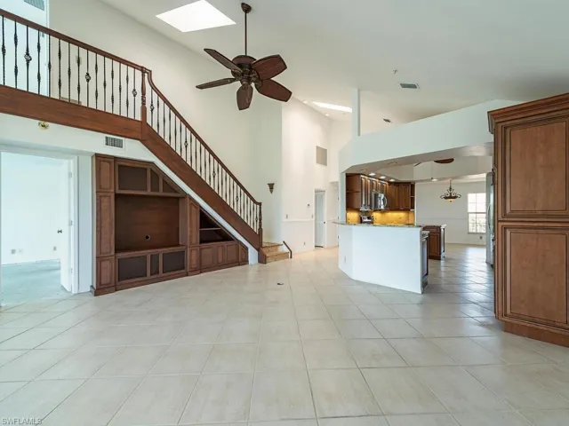 Unfurnished living room featuring a skylight, a towering ceiling, light tile patterned floors, and ceiling fan