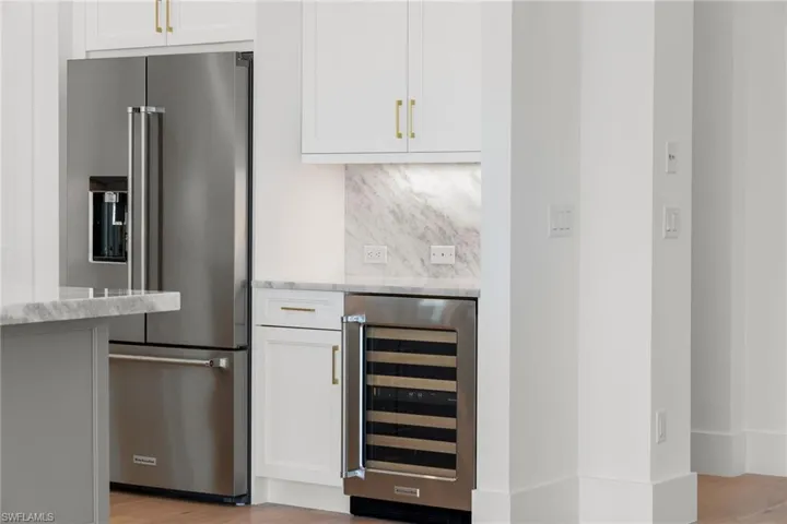 Kitchen with high quality fridge, wine cooler, light wood-style flooring, light stone counters, and tasteful backsplash