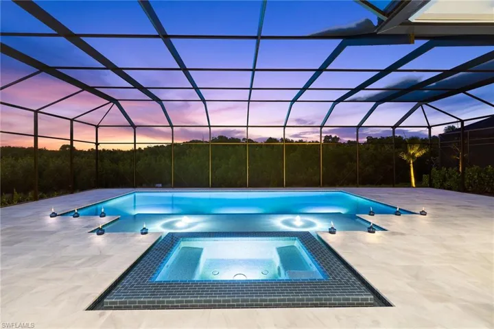 Pool at dusk featuring a patio, a pool with connected hot tub, and glass enclosure