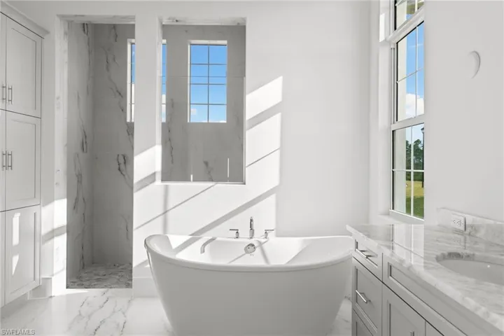 Full bath with marble tiled flooring, a freestanding tub, vanity, and a marble finish shower