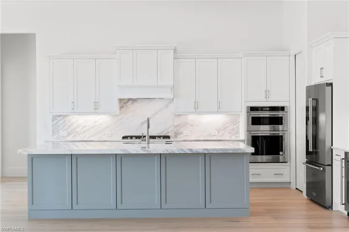 Kitchen featuring stainless steel appliances, light stone counters, white cabinets, and tasteful backsplash