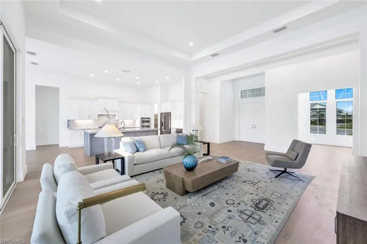 Living room with a tray ceiling, light wood-type flooring, recessed lighting, and a high ceiling