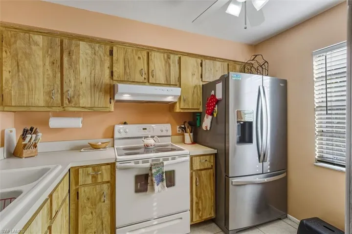 Kitchen featuring electric range, stainless steel fridge, light countertops, and under cabinet range hood