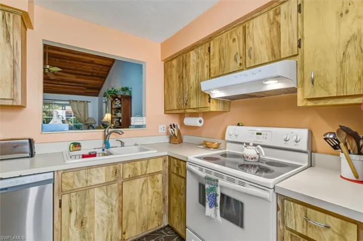 Kitchen with electric stove, stainless steel dishwasher, under cabinet range hood, light countertops, and vaulted ceiling
