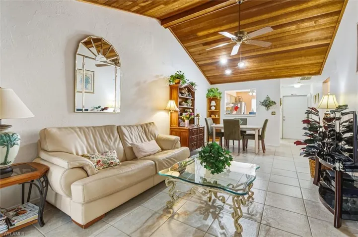 Living area featuring wooden ceiling, vaulted ceiling, a ceiling fan, tile patterned flooring, and a textured wall