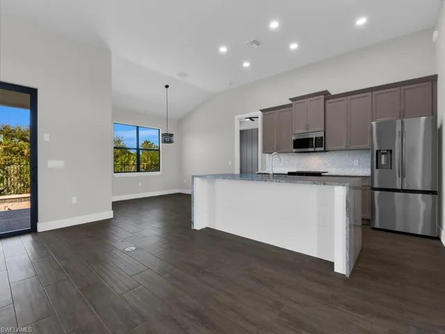 Kitchen featuring light stone counters, stainless steel appliances, a center island with sink, backsplash, and lofted ceiling