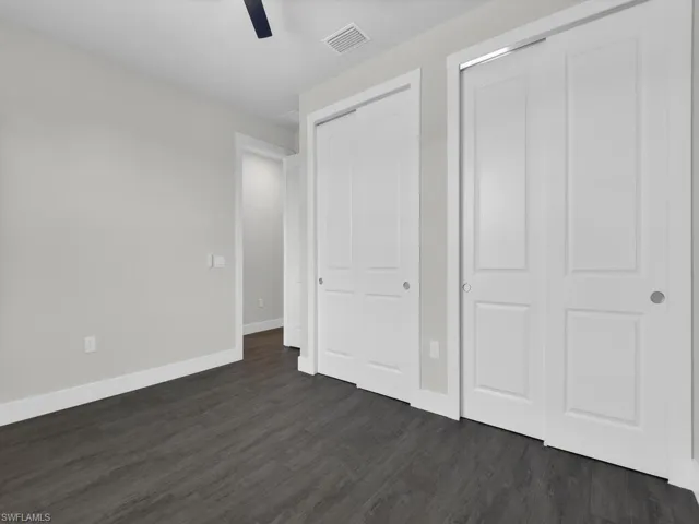 Unfurnished bedroom featuring dark wood-style flooring, two closets, and ceiling fan