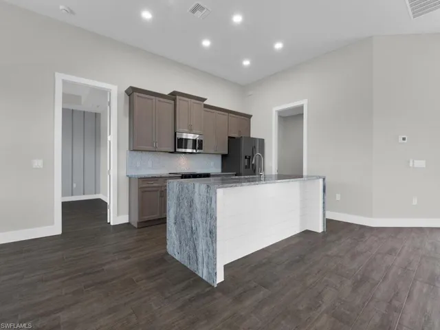 Kitchen with light stone countertops, dark wood finished floors, a kitchen island with sink, stainless steel appliances, and recessed lighting