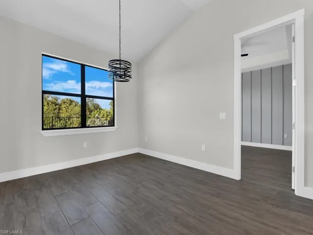 Unfurnished room with lofted ceiling, dark wood-type flooring, and hanging lights