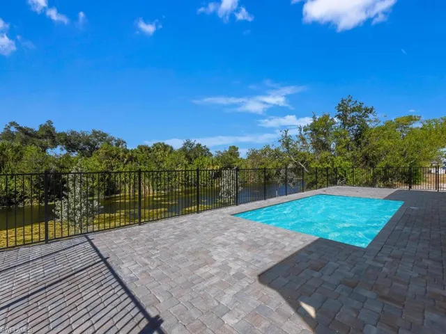 View of pool featuring a fenced backyard, patio surround, view of scattered trees, and a water view
