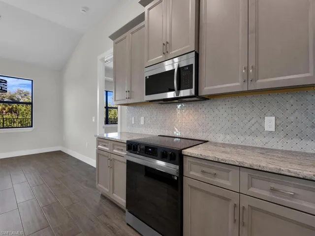 Kitchen with black electric range oven, stainless steel microwave, lofted ceiling, light stone countertops, and tasteful backsplash