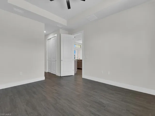 Empty room featuring a tray ceiling, dark wood-style flooring, and ceiling fan