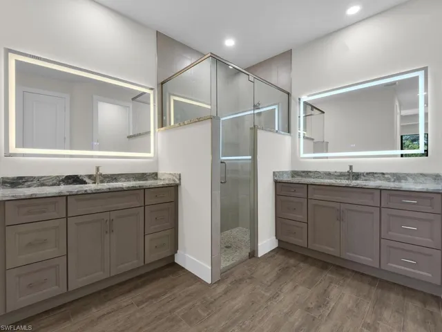 Full bathroom with a stall shower, dark wood-style flooring, two vanities, and recessed lighting