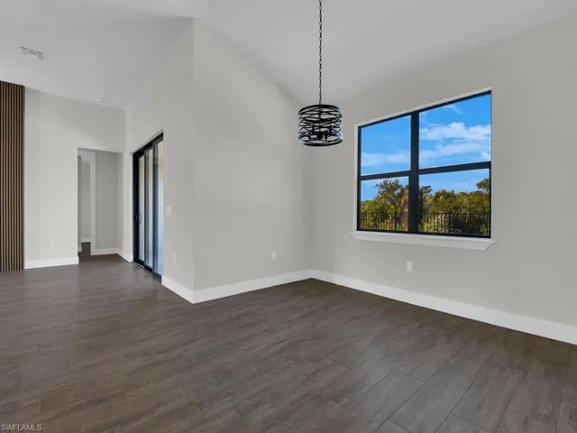 Unfurnished room with dark wood-style flooring, a chandelier, and lofted ceiling