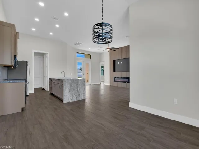 Kitchen featuring open floor plan, hanging light fixtures, light stone counters, and dark wood-style flooring