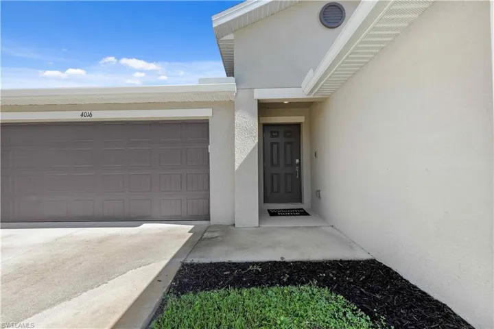 View of exterior entry with concrete driveway, an attached garage, and stucco siding