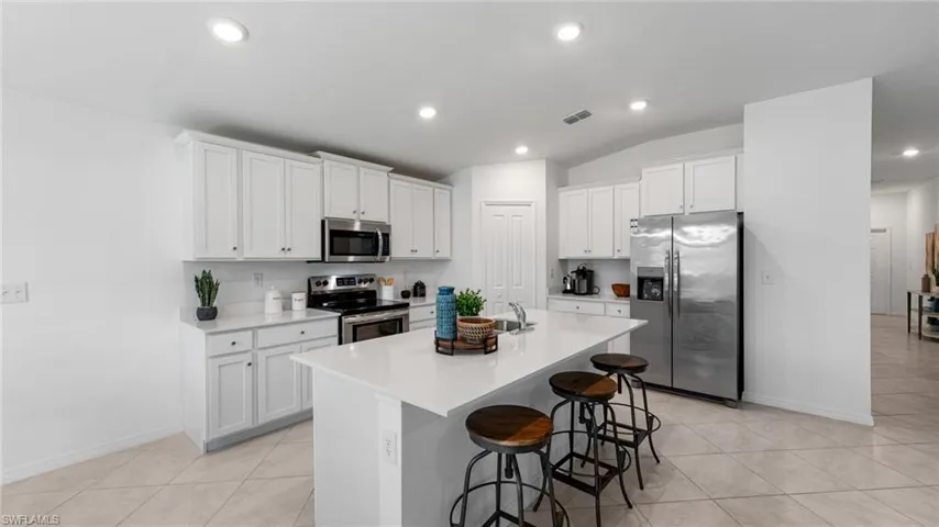 Kitchen with stainless steel appliances, white cabinetry, a kitchen bar, an island with sink, and recessed lighting
