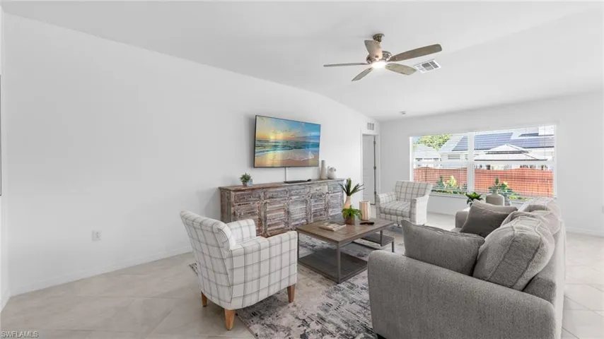 Living room with vaulted ceiling, light tile patterned flooring, and ceiling fan