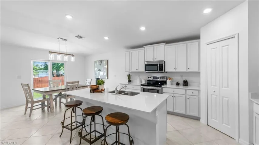 Kitchen with white cabinets, decorative light fixtures, appliances with stainless steel finishes, a kitchen island with sink, and recessed lighting