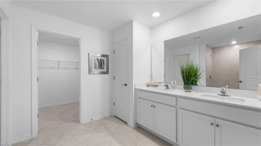 Bathroom with double vanity, tiled shower, a spacious closet, light tile patterned flooring, and recessed lighting
