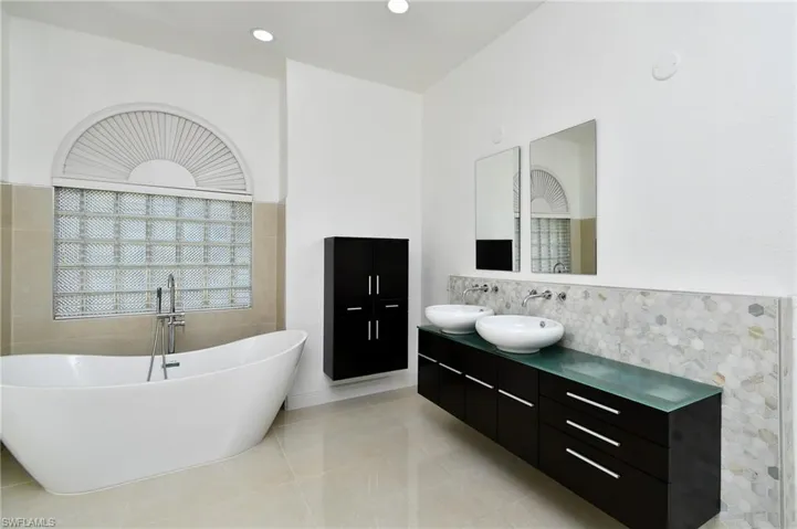 Bathroom with double vanity, a soaking tub, light tile patterned floors, tile walls, and backsplash