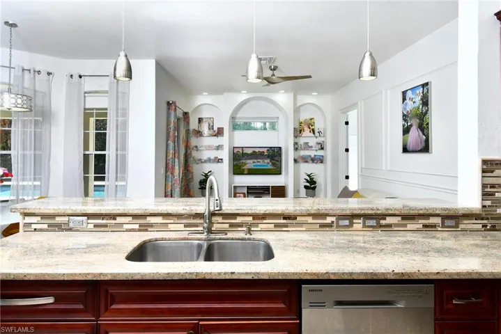 Kitchen featuring hanging light fixtures, light stone counters, dishwasher, and bold wood finish cabinetry