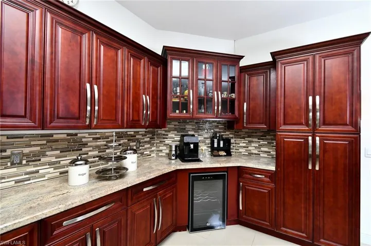 Kitchen with bold wood finish cabinets, glass fronted cabinets, wine cooler, and light stone counters