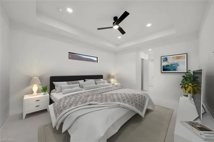Carpeted bedroom featuring a raised ceiling, recessed lighting, and a ceiling fan
