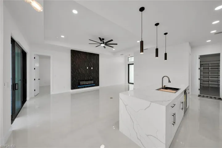 Kitchen featuring decorative light fixtures, light stone countertops, recessed lighting, white cabinetry, and an island with sink