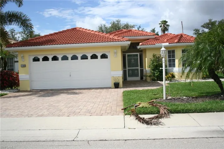 Exterior featuring a red tile roof, pale yellow stucco siding, a two-car garage with arched window accents, a paver driveway, and a screened entry