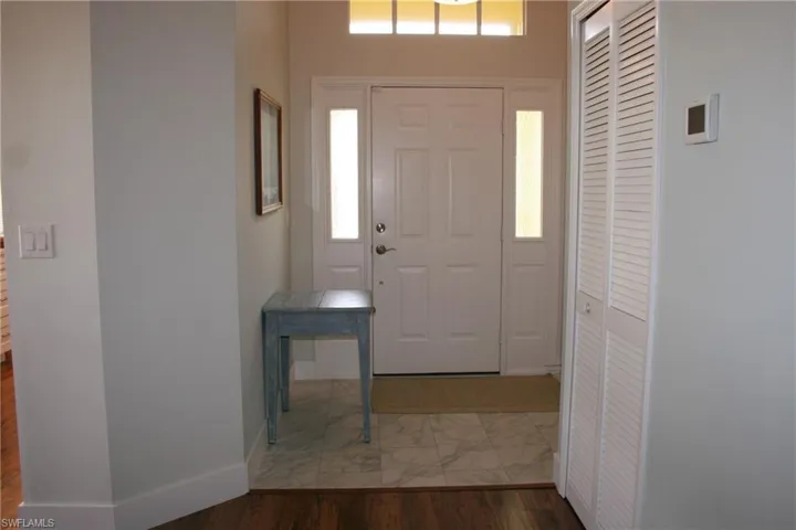 Entryway featuring a white paneled door with sidelights and transom window, bi-fold louvered closet doors, and tile flooring
