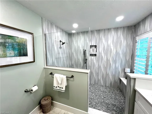 Walk-in shower with decorative tiled walls, integrated shelving, and a pebbled floor