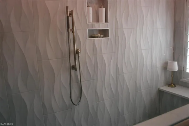 Textured shower wall tile, integrated shower niche shelving, and a handheld shower fixture