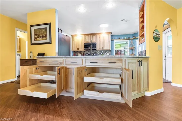 Kitchen with light brown cabinetry, open shelves, light countertops, and stainless steel microwave