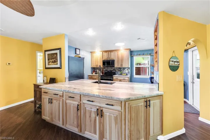 Kitchen with light brown cabinetry, backsplash, stainless steel appliances, dark wood finished floors, and arched walkways