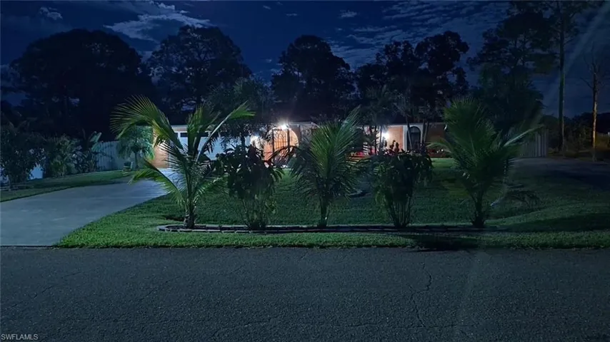 View of property hidden behind natural elements featuring a lawn and concrete driveway