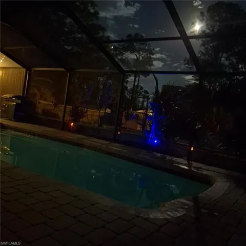 Pool at twilight featuring an outdoor pool, glass enclosure, and a patio